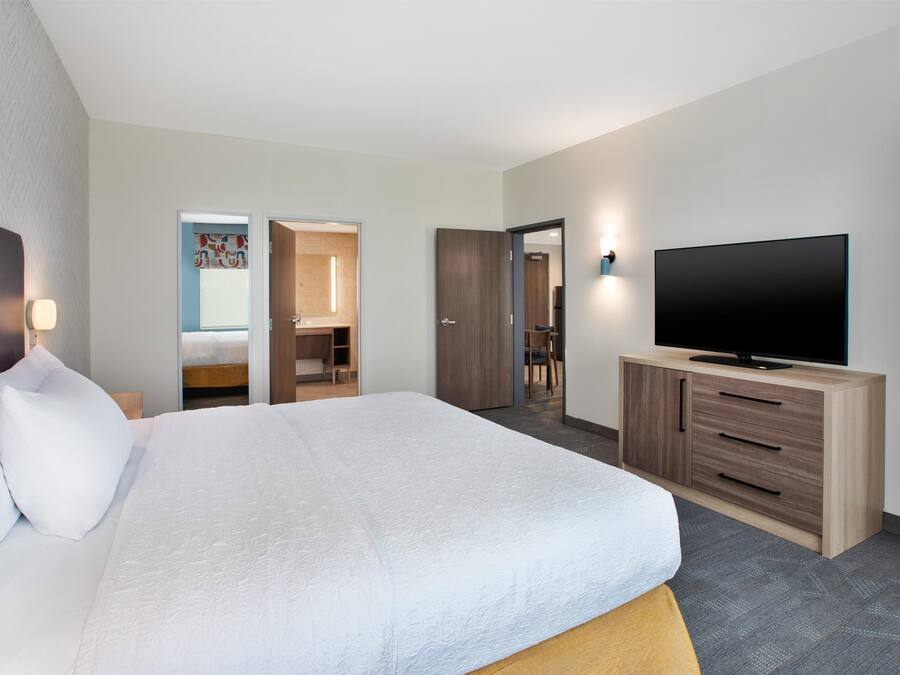 Une chambre d’hôtel avec un grand lit, un téléviseur posé sur une commode en bois et une salle de bain visible à travers une porte ouverte.