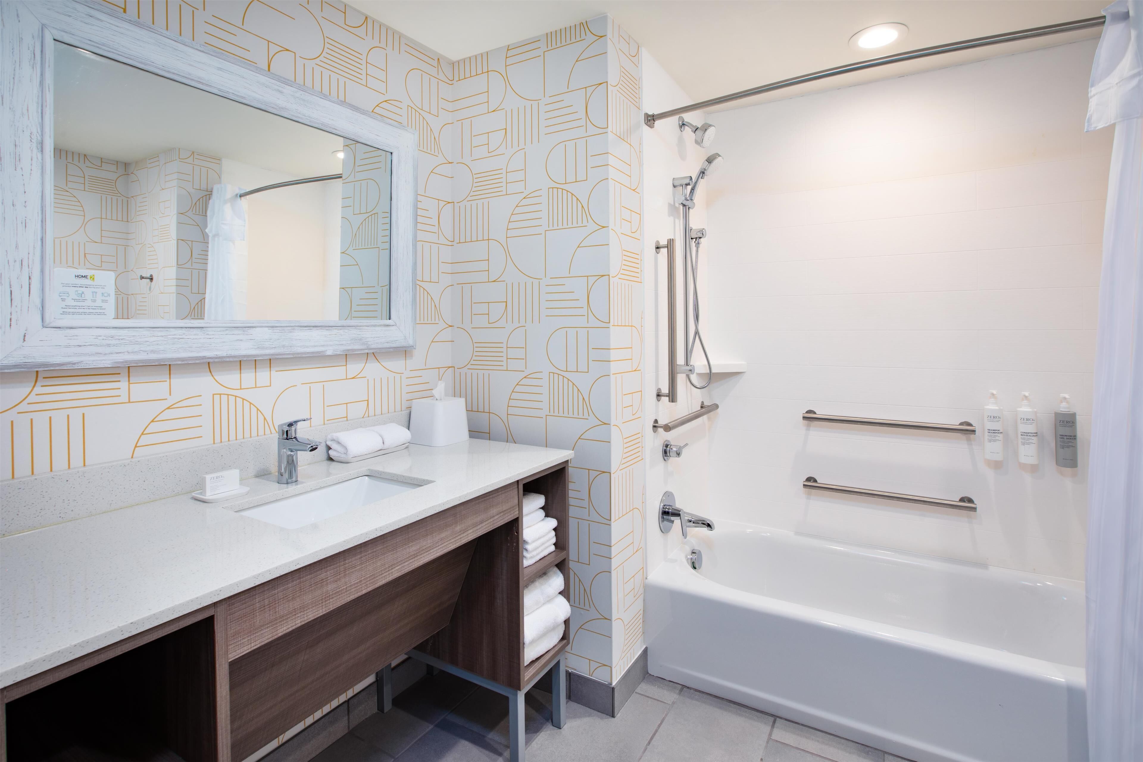 Un baño moderno con un espejo grande, un lavamanos blanco, un mueble de tocador de madera y una bañera blanca.