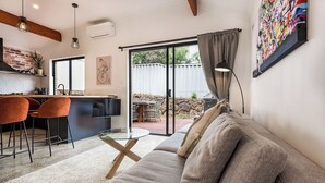 A modern living room with a sofa, a glass coffee table, and a kitchen area with a brick wall and pendant lights.