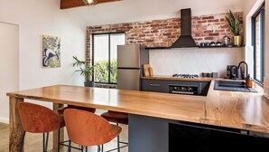 A modern kitchen with a large island, wooden ceiling beams, and a brick accent wall.