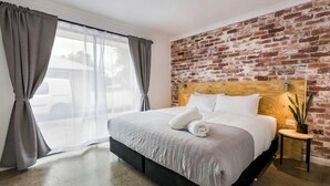 A modern hotel room with a brick wall, a large bed, and a view through a window with curtains.