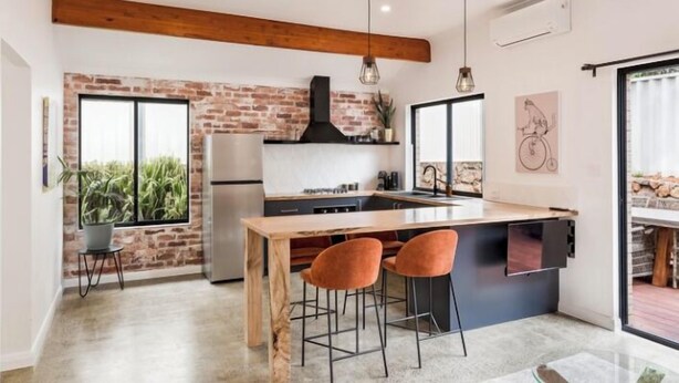 A modern kitchen with a brick wall, wooden beams, and a large island with bar stools.