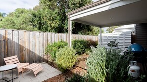 Un patio techado con cerca de madera, mobiliario exterior y un cilindro de gas.