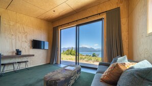 A modern room with a large window, a flat-screen TV, a sofa, and a patterned ottoman. - Tukare Lookout (Te Anau)