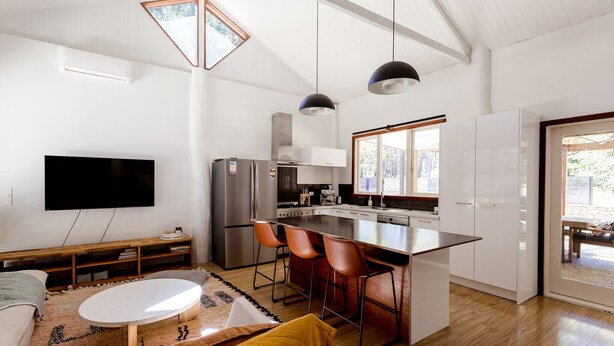 A modern kitchen with a central island, bar stools, and a large window.