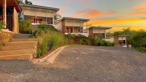 A modern two-story house with a gravel driveway and a covered outdoor seating area. - Essence of Honey Villas & Safari Boutique - Villa # 1 (Provincia de Guanacaste)