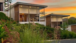 A modern two-story house with large windows, a balcony, and a view of the surrounding greenery. - Essence of Honey Villas & Safari Boutique - Villa # 1 (Provincia de Guanacaste)