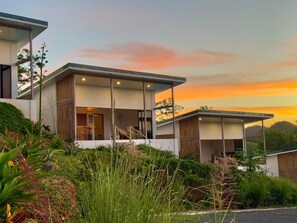A modern two-story house with large windows, a balcony, and a view of the surrounding greenery.