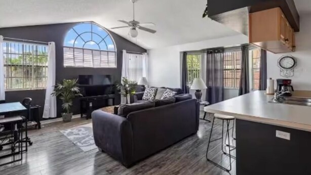 A modern living room with a dark sofa, a dining area with a table and chairs, and a kitchen with a bar area. - condo2/2 pretty Close to Disney (Kissimmee)