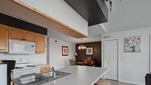 A modern kitchen with a large island, wooden cabinets, and a dining area with a chandelier. - condo2/2 pretty Close to Disney (Kissimmee)