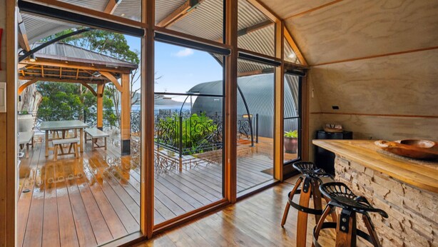 Un espacio interior amplio con terraza de madera, zona de bar con taburetes y vistas al exterior.