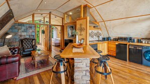 Un espacio habitable tipo tienda acogedor y bien iluminado, con una mesa de comedor de madera, sillas de cuero y una pared decorativa de piedra.