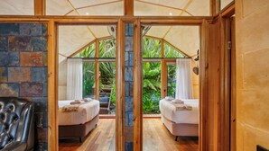 Una habitación con dos camas, una pared de piedra, suelo de madera y vistas al exterior con vegetación.