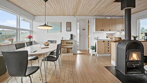 A modern kitchen with a wood-burning stove, a dining area with a large table and chairs, and a view of the outdoors through large windows. - Awesome home in Ebberup with WiFi (Ebberup)
