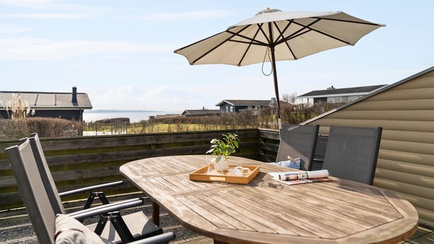 A wooden table with a tray of snacks and a drink, an umbrella, and a view of the sea and houses in the background. - Awesome home in Ebberup with WiFi (Ebberup)