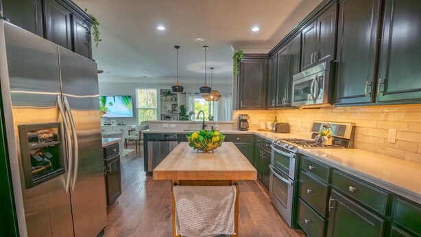 Una cocina moderna con armarios oscuros, electrodomésticos de acero inoxidable y una isla de madera con un bol de fruta.