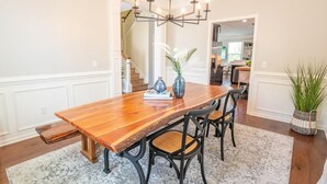 Un comedor con mesa de madera, sillas negras, una araña y una planta en maceta.