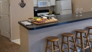 A kitchen with a central island, white cabinets, a microwave, and a refrigerator. There are three wooden stools at the island. - Creekside Condo w/ Pool & Beach Club #118 (Bellaire)