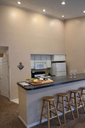 A kitchen with a central island, white cabinets, a microwave, and a refrigerator. There are three wooden stools at the island. - Creekside Condo w/ Pool & Beach Club #118 (Bellaire)