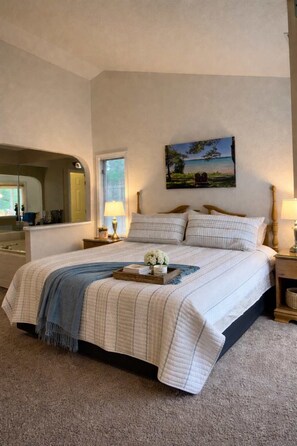 Une chambre à coucher avec un grand lit, une table de chevet, une commode, un miroir et une fenêtre.