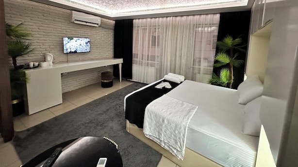 A modern hotel room with a bed, a TV on the wall, a desk, and a window with curtains.