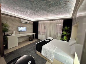 A modern hotel room with a bed, a TV on the wall, a desk, and a window with curtains. - Grani Butik Otel (Bursa)