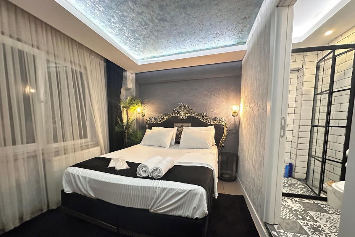 A modern hotel room with a large bed, a skylight, a shower area, and a view of the cityscape.