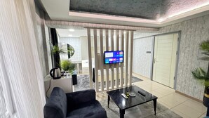 A modern living room with a black sofa, a coffee table, and a flat-screen TV mounted on a wall. There is a sliding door leading to another room.