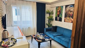 A modern living room with a blue sofa, a coffee table with snacks, a TV, and a window with sheer curtains.