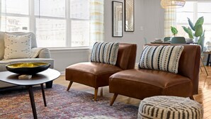 Un salon moderne comprenant un canapé, deux fauteuils en cuir, une table basse et un coin repas avec une table et des chaises.