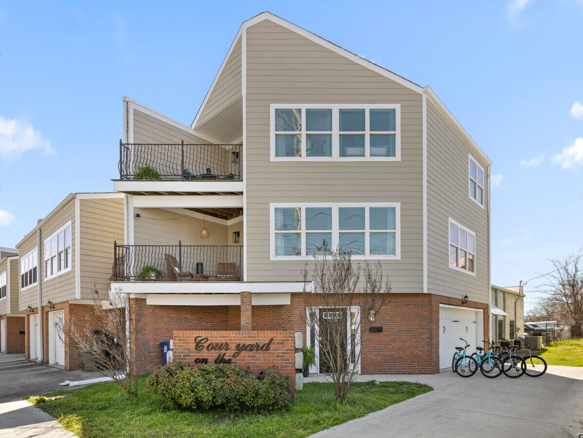 A two-story apartment building with a brick facade, a balcony on the upper floor, and a garage with bicycles parked outside.