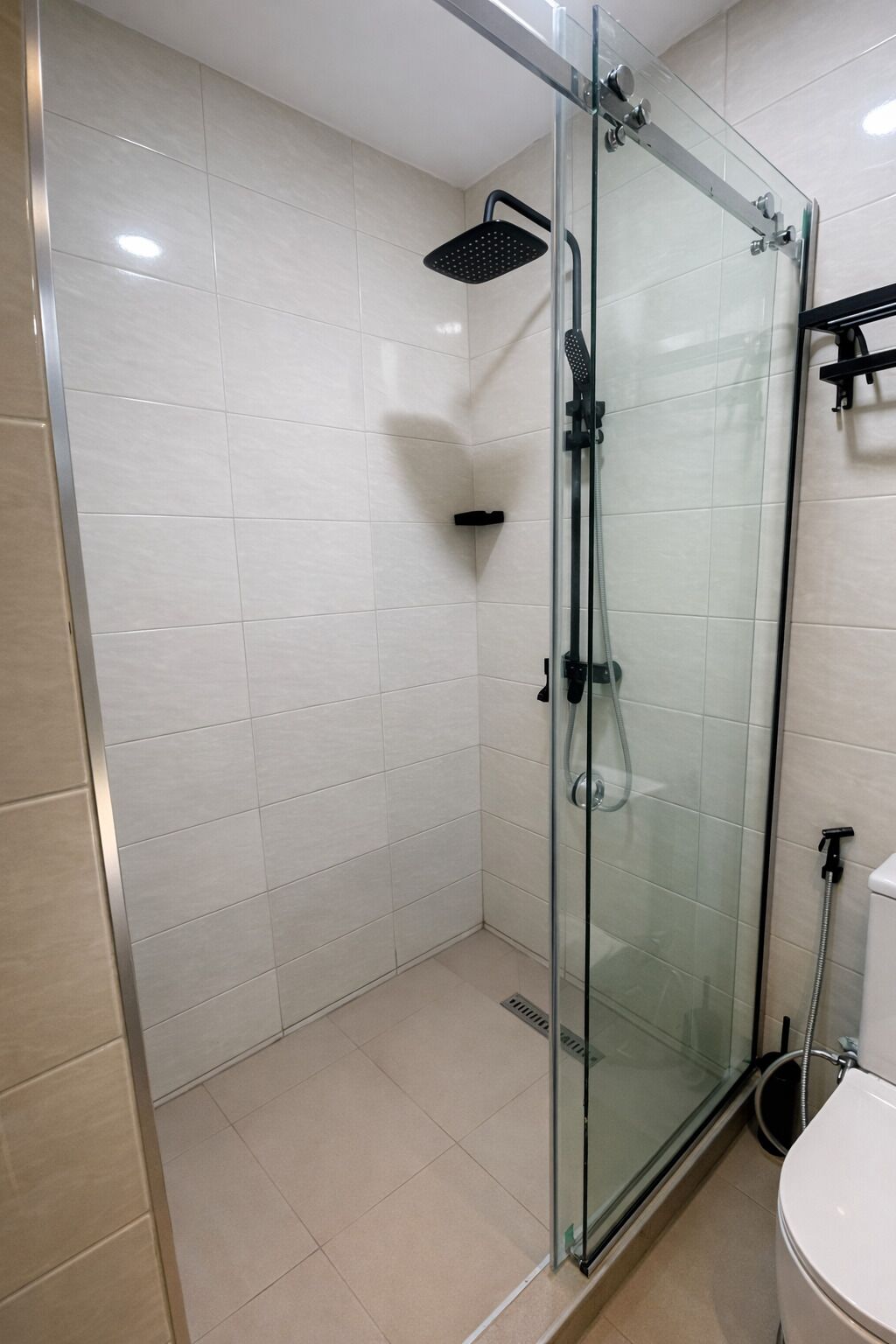A glass-enclosed shower with a handheld showerhead, a glass door, and a white tiled wall.