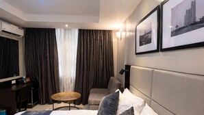 A hotel room with a large bed, a desk, a chair, a small round table, and two framed pictures on the wall. - Five Clover Inn Abijo (Lekki)