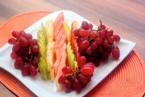 Un plato blanco con uvas rojas, rebanadas de manzana y sandía sobre un camino de mesa naranja.
