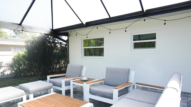 Un patio cubierto con muebles blancos, incluyendo sofás y una mesa, y una guirnalda de luces.