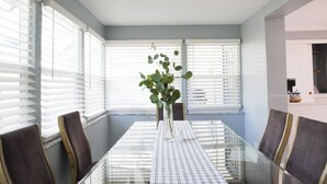 Un comedor con una mesa de vidrio, sillas y un florero con plantas verdes.