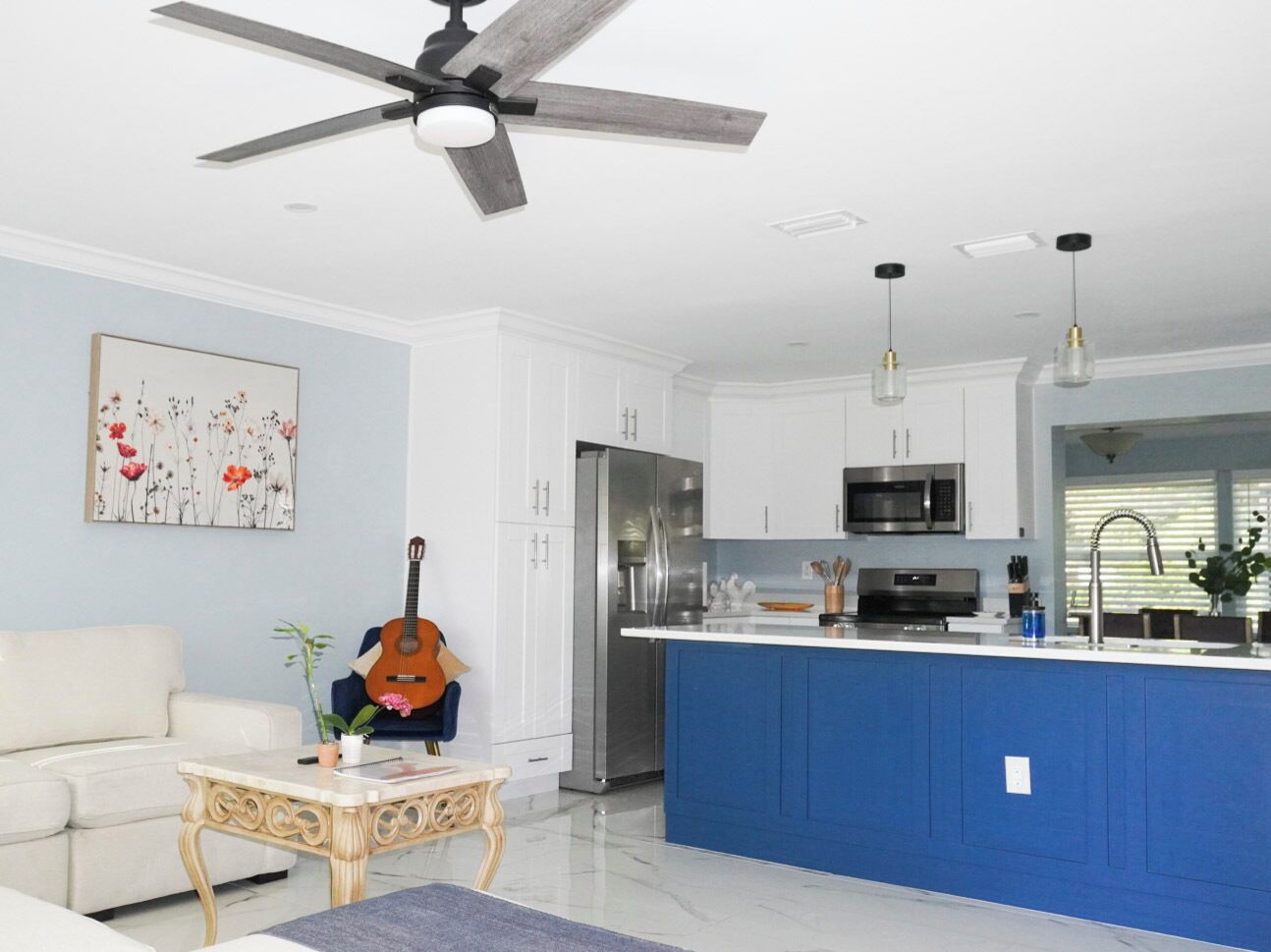 Una cocina moderna con armarios blancos, una isla azul, electrodomésticos de acero inoxidable y un ventilador de techo.