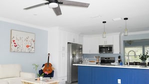 Una cocina moderna con armarios blancos, una isla azul, electrodomésticos de acero inoxidable y un ventilador de techo.