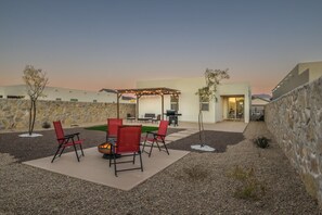 An outdoor patio with a fire pit, red chairs, and a pergola with string lights.