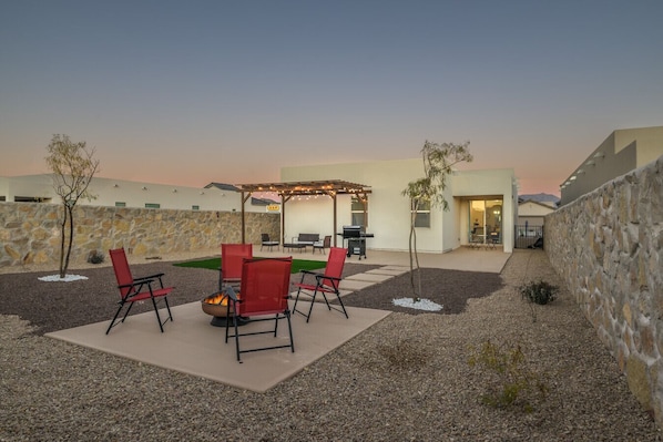 Un patio al aire libre con un hogar para fuego, sillas rojas y una pérgola con luces colgantes.