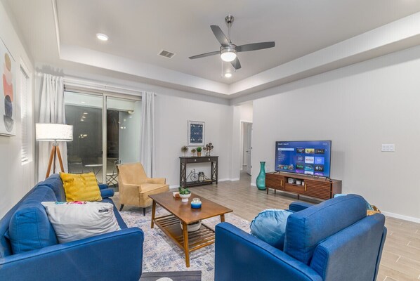 A modern living room with a blue sofa set, a wooden coffee table, and a television displaying streaming services.