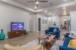 Una sala de estar moderna con un televisor de pantalla plana, un sofá azul, una mesa de centro de madera y un sillón color beige.