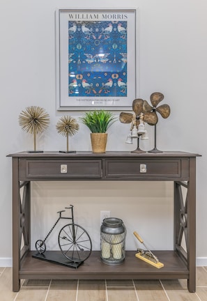 Una consola de madera oscura con una obra enmarcada, objetos decorativos y una bicicleta.