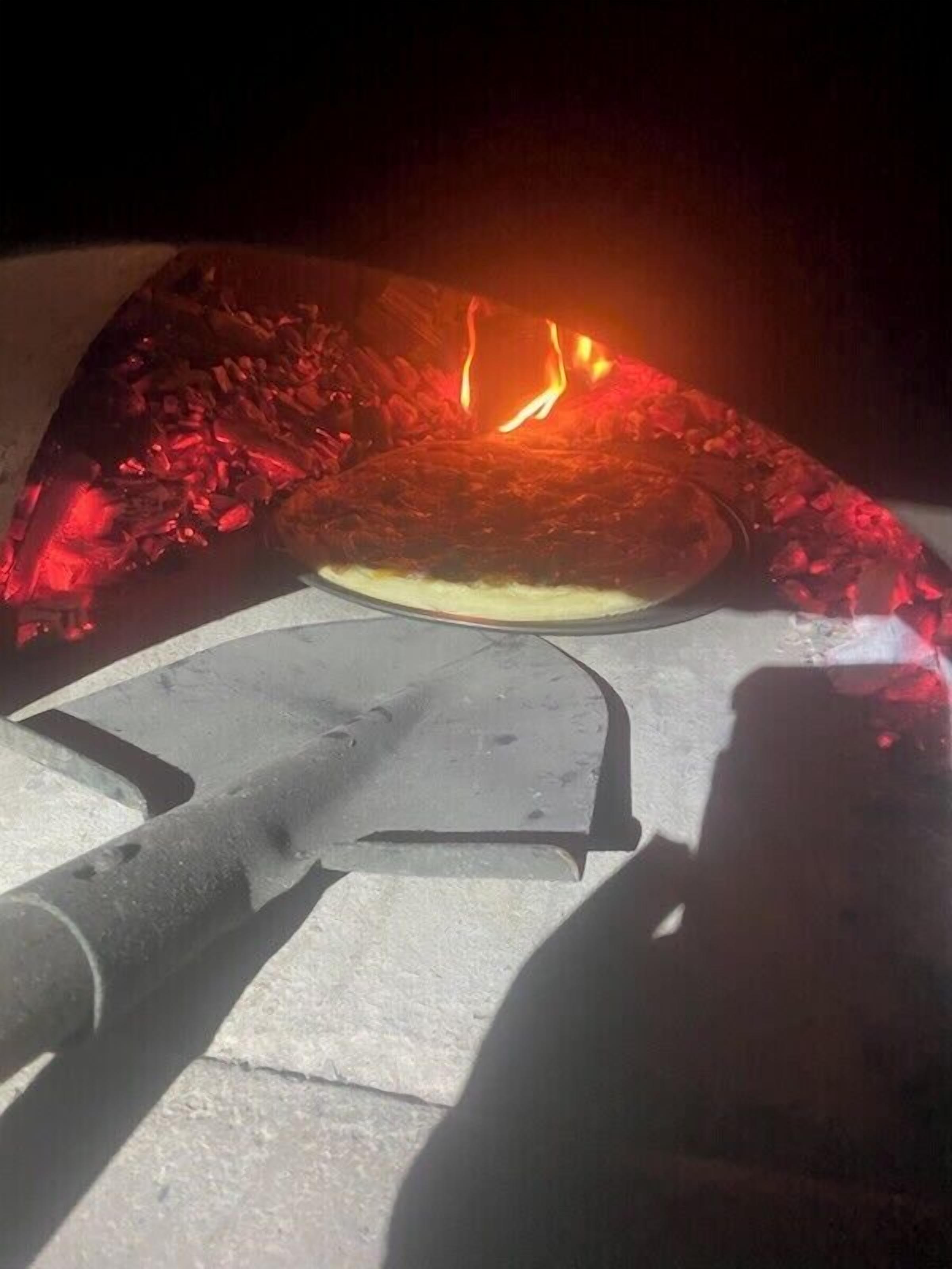 Una pizza en horno de leña, con un cortador de pizza y una pala para pizza.