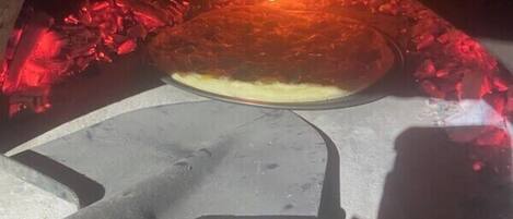 Una pizza en horno de leña, con un cortador de pizza y una pala para pizza.