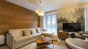 A modern living room with a wooden wall, a sofa, a coffee table, a TV, and a painting of a forest. - ☆☆☆ 3 Vallées & cycling – Cosy 6 to 8 in the Alps (Orelle)