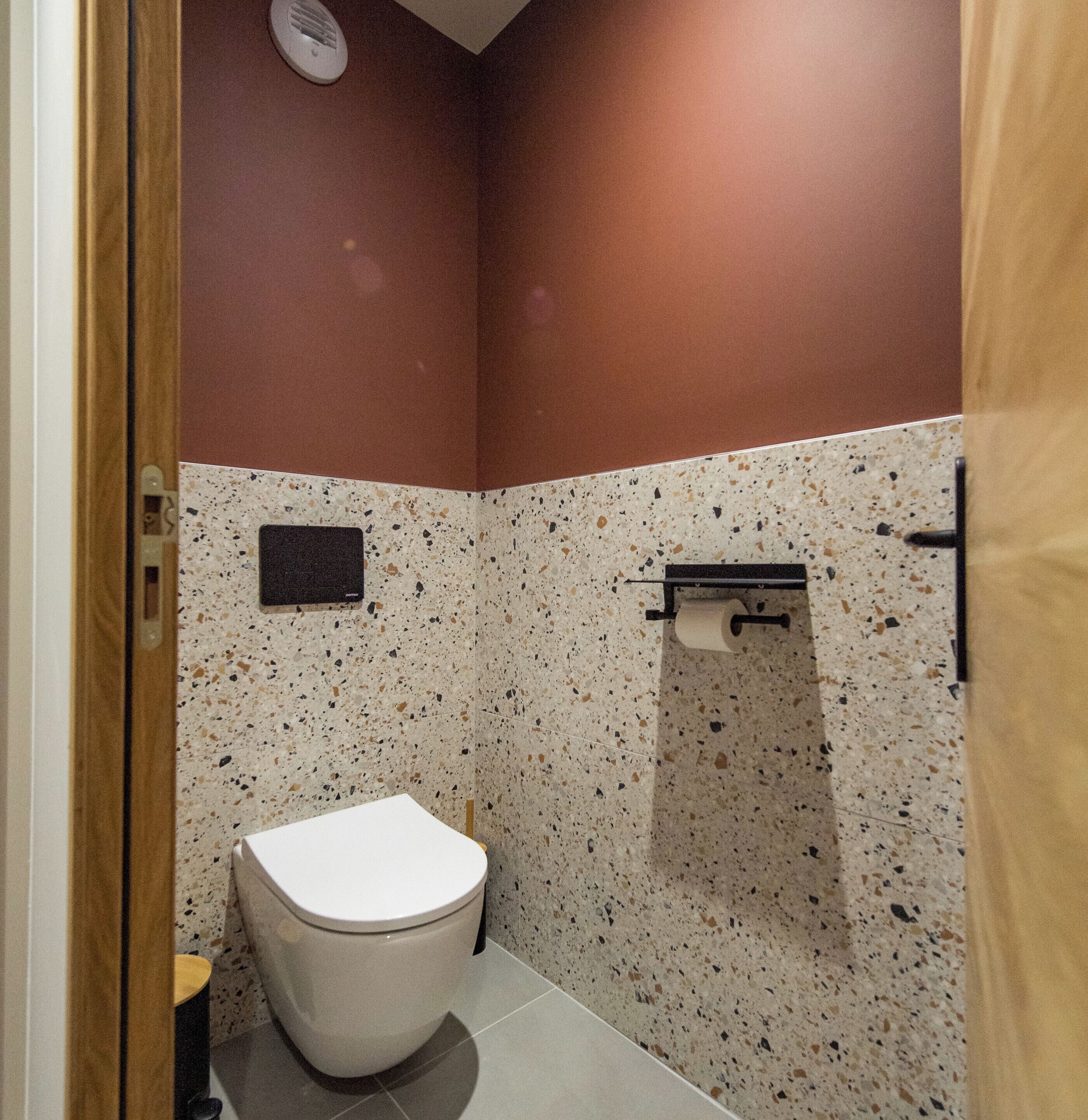 A small, compact bathroom with a white toilet, a wall-mounted toilet paper holder, and a small shelf.