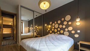 A modern bedroom with a large bed, wooden flooring, a mirror, and a wall decorated with circular wooden slices. - ☆☆☆ 3 Vallées & cycling cols – Cosy 6 to 8 stay (Orelle)