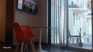 A modern hotel room with a Galaxy A23 smartphone on the table, a red chair, and a balcony with a view of the city.