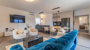 Un salon moderne avec un grand canapé bleu, une table basse en marbre et un téléviseur fixé au mur.